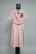 Pink trench coat with a floral accessory on a mannequin against a neutral background.